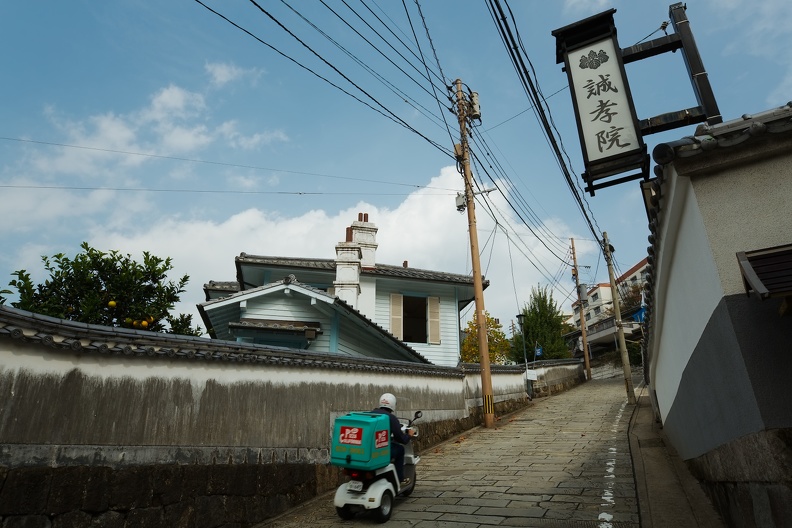 Livreur de pizzas remontant la Dutch Slope de Nagasaki en scooter à trois roues