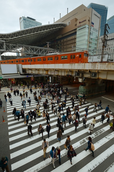Train entrant en gare d'Osaka et piétons traversant le passage clouté